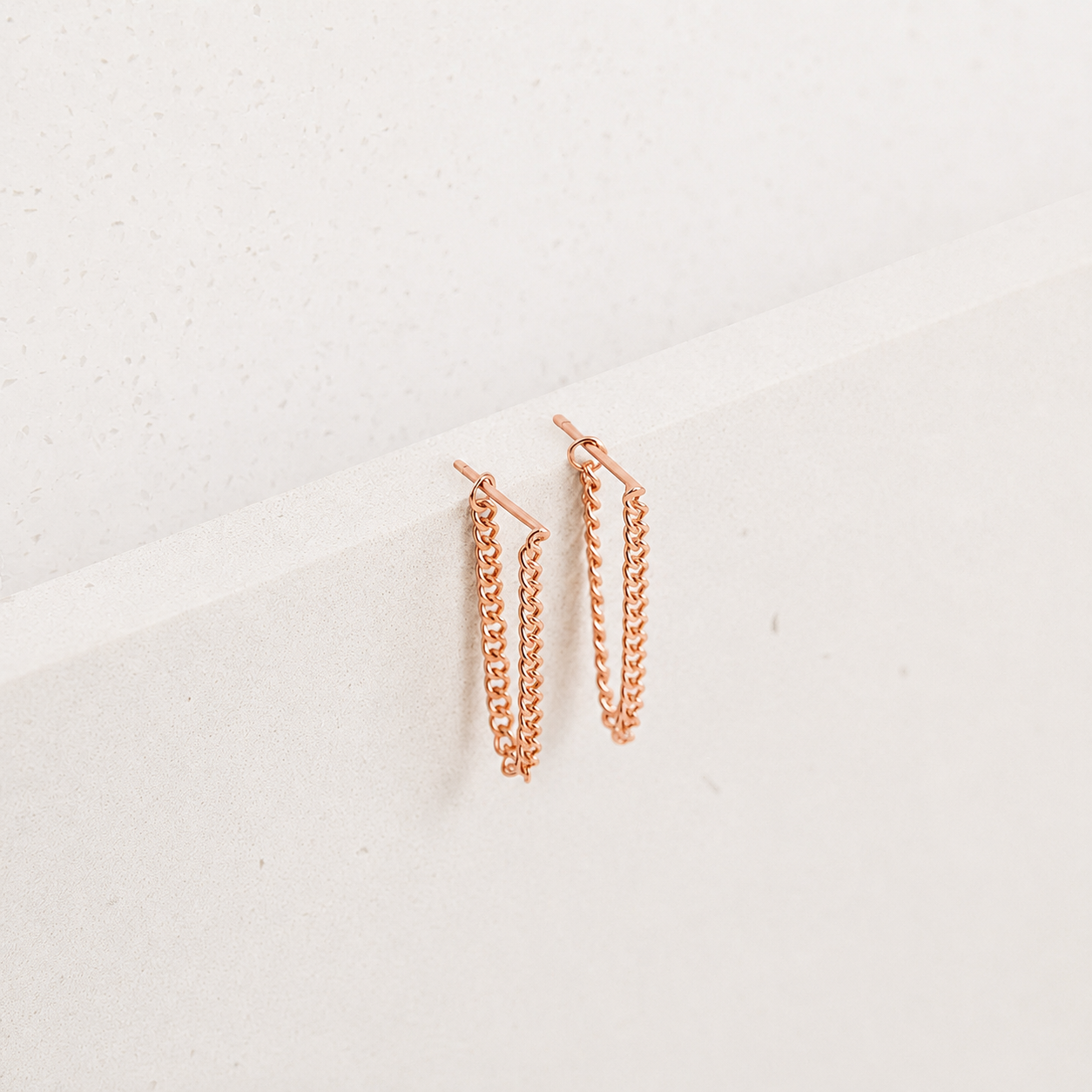 Rose gold chain earrings on a light gray background